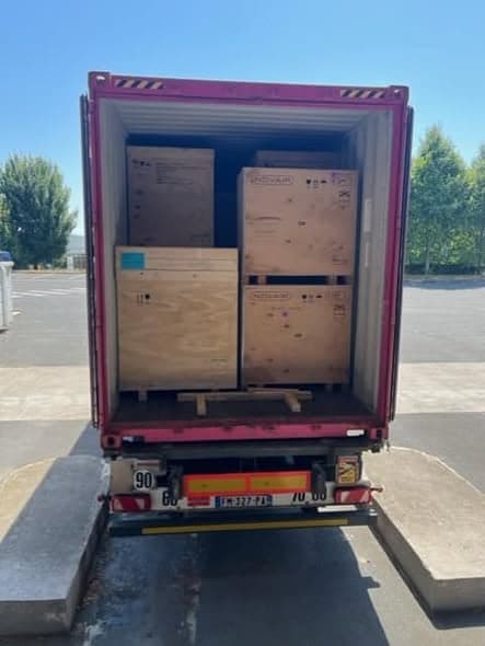 The open rear of a shipping container holding four large crated oxygen plants, two of them stencilled Novair, on a loading apron in France.