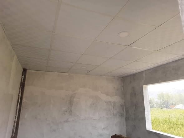 The interior of a finished classroom with a tiled suspended ceiling, recessed light fittings and a window onto a green field.