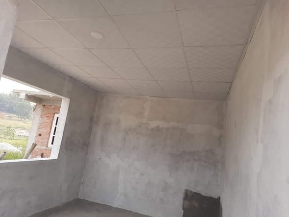 Another unfinished room with a suspended ceiling in place and an unglazed window framing brickwork and fields outside.