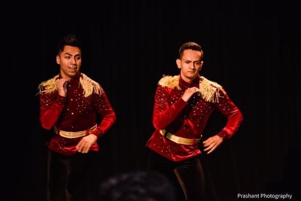 Two dancers in red sequinned costumes with gold epaulettes performing on a darkened stage
