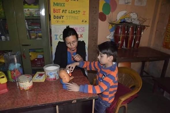 A teacher and a boy at a table working together on a soft doll, in a room hung with alphabet charts and posters.