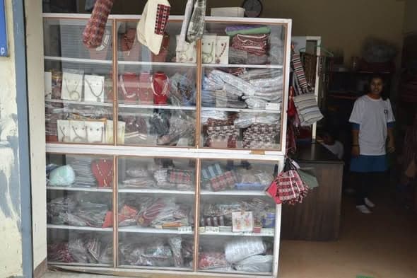 Glass-fronted cabinets at the school stocked with handmade bags, jewellery, woven cloth and knitted goods, with a student standing beside them.