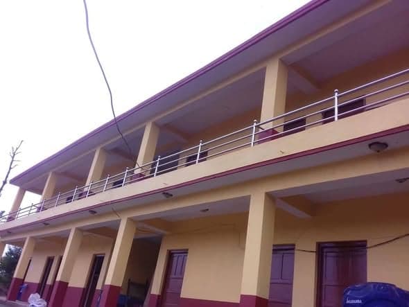 The long facade of the finished school, colonnaded on both floors, with a steel balcony rail and a cable running up to the roof.