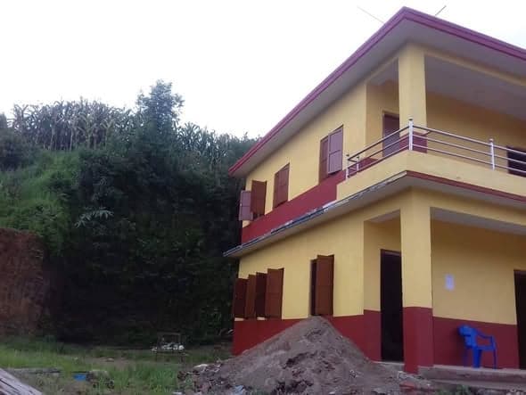 The school seen from the side, standing against a steep green hillside with a mound of sand at its base.