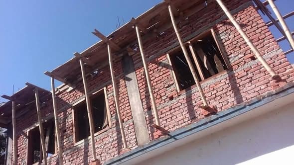 Brick walls of a new upper storey rising behind timber scaffolding under a clear sky.
