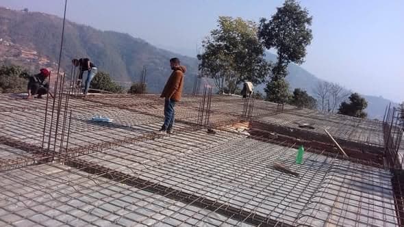Workers on a rooftop tying a grid of reinforcing bar for a concrete slab, with hills behind.