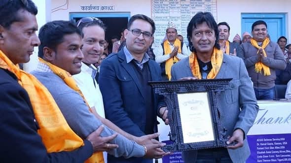 A framed certificate is presented to a man in a grey coat as a line of people in yellow scarves applaud.