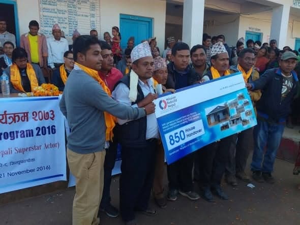 Men in topis hold one end of a printed 850 House Handover board beside a banner for the 2016 handover programme.