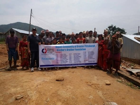 About thirty villagers and children stand behind a long banner naming the Nepali Community of Greater Pittsburgh and Brother's Brother Foundation.