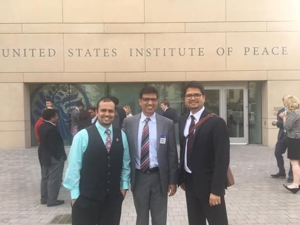 Three men in suits stand together outside the entrance of the United States Institute of Peace.