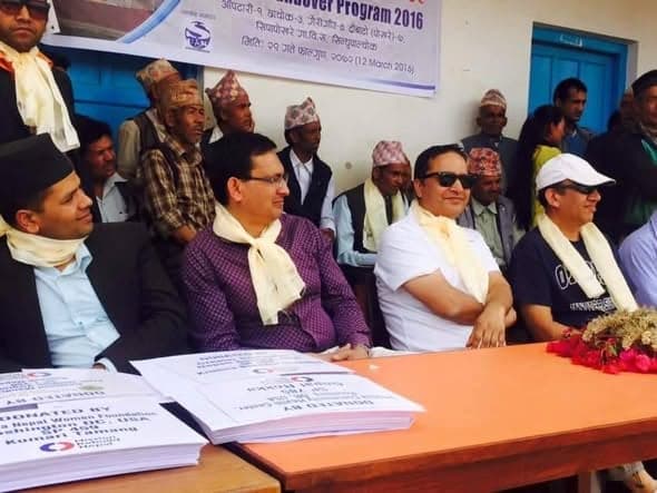 Guests seated at a table under a banner reading Handover Program 2016, Sipapokhare, Sindhupalchowk, with stacks of documents in front of them.