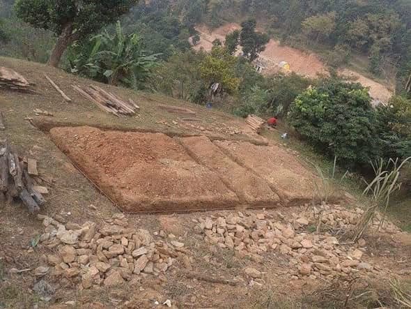 Three levelled earth platforms cut into a steep hillside, with stacked timber and heaps of stone waiting beside them.
