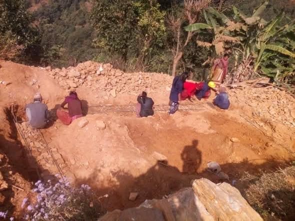 Six people crouch along string lines marking out foundations on freshly dug red earth.