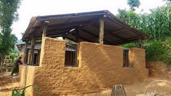 A newly mud-plastered house with barred windows and a timber-framed corrugated roof, a worker at the far corner.