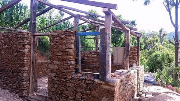 A stone house shell with a timber roof frame, an internal brick pillar and open window and door spaces.