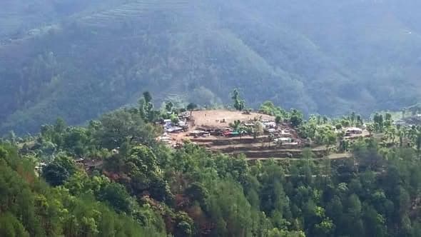 A distant view of a hilltop settlement of tents and shelters surrounded by forest and terraced fields.