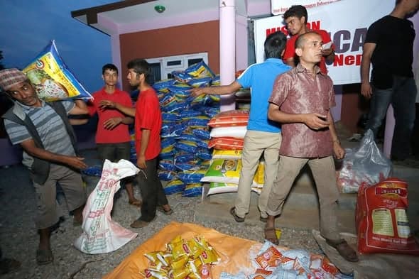 Volunteers passing sacks of rice and packaged food onto a stacked pile outside a building at dusk.