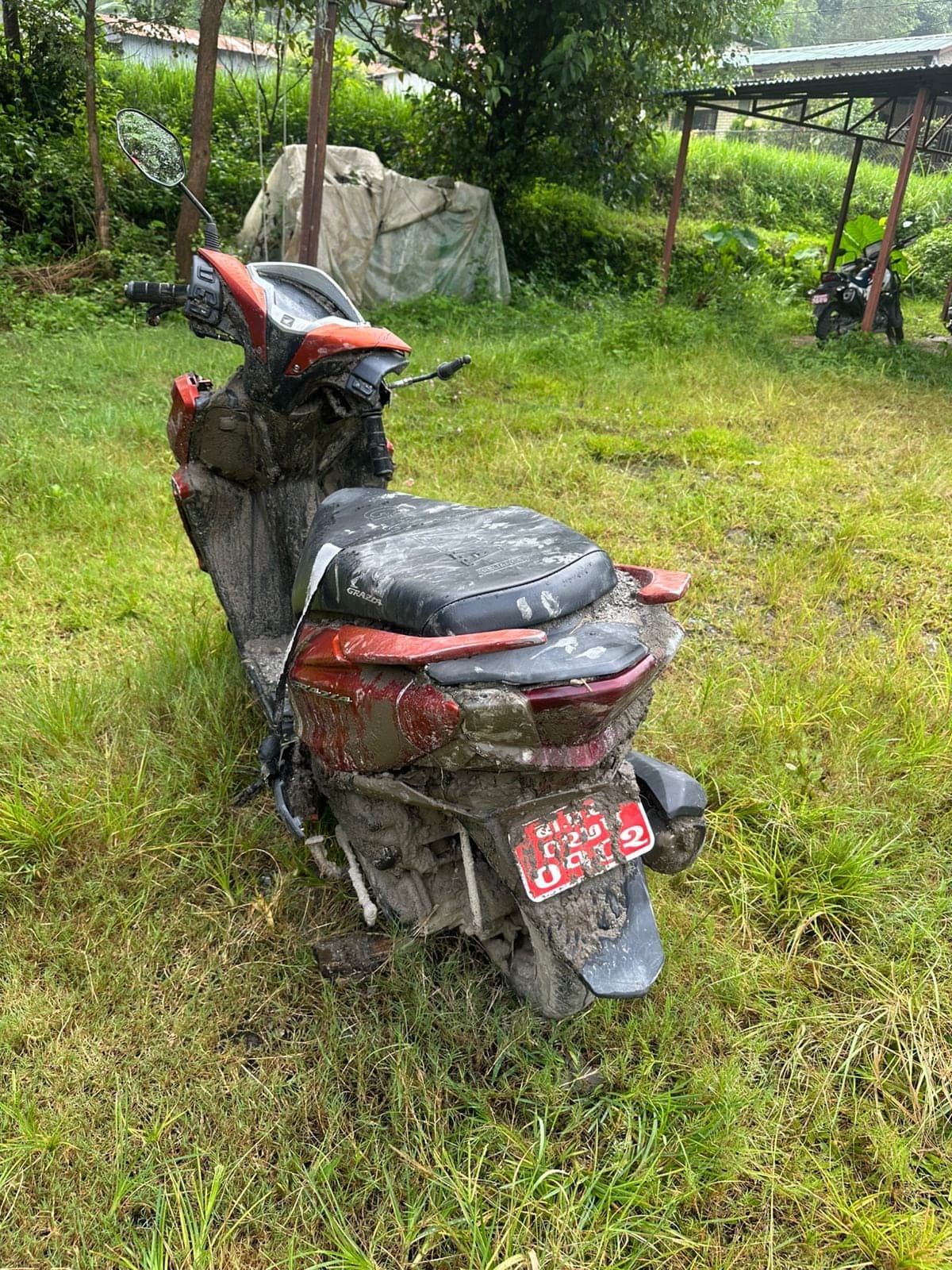 A scooter standing in long grass, caked to the seat in dried grey flood silt.