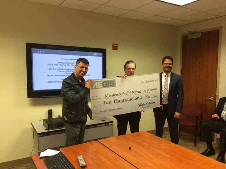 Three men holding an oversized presentation cheque for ten thousand dollars made out to Mission Rebuild Nepal in a corporate meeting room